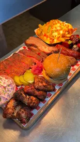 A promotional video for Tex's Smoke & Grill showcasing their 'build your own BBQ tray' offering, featuring close-up shots of brisket, ribs, sausages, and burgers being sliced and plated.