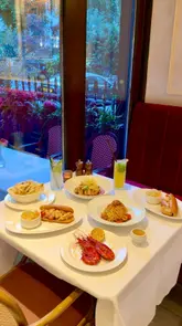 The video presents a montage of AVI Bistrot Américain, highlighting its elegant, Parisian-inspired interior and a variety of dishes including lobster rolls, pasta, and prawns. The creator is shown enjoying the space, emphasizing the venue's suitability for various dining occasions from breakfast to dinner.