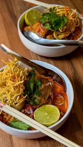 A couple attends a private Thai cookery workshop, learning to make dishes like pork toast, Thai green chicken curry, and Khao Soi. The video documents the process of preparing ingredients, cooking, and plating the final dishes in a home kitchen setting.