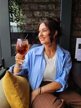 A high-quality lifestyle portrait of a woman enjoying a cocktail in a cozy, brick-walled venue. The image effectively captures the warm, inviting atmosphere of the space, making it feel like an appealing destination for social gatherings.