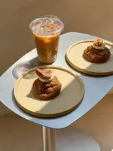 A high-quality, well-lit photograph of two gourmet cookies and an iced coffee on a minimalist metallic table, showcasing the product's texture and presentation.