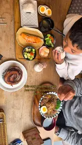 A video review of Mitsuba, a Japanese cafe in West London, featuring a mother and son trying various menu items including bento boxes, rice bowls, pastries, and cakes. The video highlights the cozy interior, specifically the tatami seating area, and provides a glimpse into the dining experience.