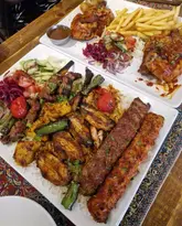 A top-down, slightly tight shot of two large platters featuring a variety of grilled meats, including skewers, chicken, and lamb, served alongside rice, salad, and fries.