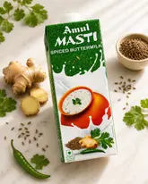 A high-quality, professional product shot of an Amul Masti Spiced Buttermilk carton, artfully arranged on a marble surface with fresh ingredients including ginger, cumin seeds, cilantro, and a green chili.