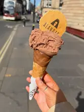 A close-up, handheld shot of a chocolate ice cream cone featuring a branded wafer, captured against a blurred city street background.