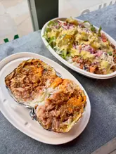A top-down shot of a halved burrito and a burrito bowl, likely taken in a fast-casual restaurant setting. The lighting is natural and even, highlighting the textures of the food.