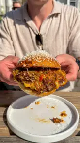 A creator visits The Edinburgh pub in Newington Green to review the burgers and spice bag served by Addie's kitchen. The video features close-up shots of the food, the venue's interior and exterior, and the creator's reaction.