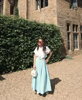 A lifestyle shot featuring a creator posing in front of a historic stone building, likely at a hotel property. The image captures a bright, sunny day in a countryside setting.