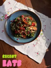 A top-down, overhead shot of a home-cooked Middle Eastern-inspired dish featuring grilled aubergine, halloumi, and pomegranate, presented on a decorative embroidered cloth.