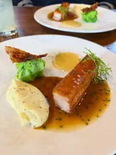 A high-quality, close-up shot of a slow-cooked pork belly dish served with grain mustard mash, hispi cabbage, and a cider sauce, captured at a restaurant.