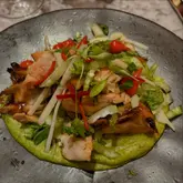 A top-down, overhead shot of a chicken dish served on a green sauce, likely taken in a restaurant setting.