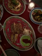 A top-down, dimly lit shot of a table filled with Cantonese dishes, including sesame-crusted prawn toast, tofu, and cucumber salad, set in a restaurant with a moody, candlelit atmosphere.