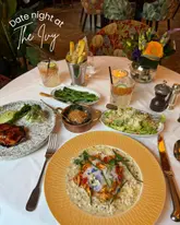 A flat-lay photograph of a dinner table at The Ivy, featuring a variety of dishes including lobster risotto, salmon, sides, and cocktails.