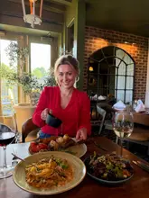 A high-quality, engaging lifestyle shot featuring a diner at an Italian restaurant. The image captures a dynamic moment of the creator pouring sauce onto a steak, which adds movement and appetite appeal. The composition is well-balanced, focusing on both the person and the food, with a shallow depth of field that keeps the subject sharp while softening the background.
