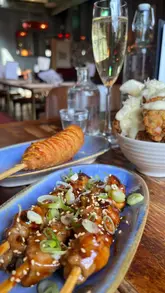 A short, fast-paced review of Korean Dinner Party in Kingly Court, London, highlighting their bottomless brunch offering. The video features close-up shots of various fusion dishes including a cheese-filled corn dog, chicken skewers, and a sizzling beef stone pot, set to music with text overlays explaining the offer.