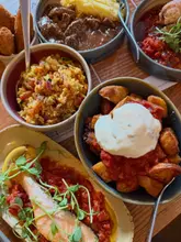 A top-down, flat-lay shot of a table filled with a variety of tapas dishes, including salmon, patatas bravas, and various meat and vegetable sides.
