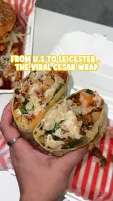A short, high-energy clip showcasing a chicken caesar wrap being opened and drizzled with sauce. The video focuses entirely on the food item, highlighting the texture and ingredients to generate interest in the new menu item at the venue.
