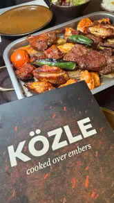 A montage-style video showcasing a variety of Turkish dishes and drinks at a restaurant called KÖZLE. The video features close-up shots of mezze, a large mixed grill platter, and a dessert selection, accompanied by background music.