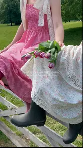 A group of friends in cottage-core attire enjoy a picnic and visit a picturesque country venue. The video features shots of them posing, taking photos, drinking champagne, and eating cake in a garden and an indoor dining area.