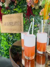 A shot of three cocktails on a reflective table in front of a green wall at a rooftop venue.