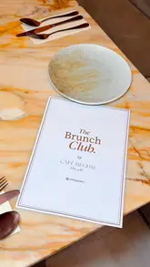 A polished promotional video showcasing the interior and brunch menu of The Brunch Club by Café Begum. The video features a variety of dishes including steak and eggs, a full breakfast, and French toast, alongside mocktails, set within a stylish, neutral-toned venue.