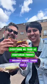 A couple visits Broadway Market in London to sample various vegetarian and vegan street food offerings, including Japanese onigiri, Indian samosas, Indonesian jackfruit rendang, iced chai, masala dosa, and Egyptian coffee. The video provides a quick review of each item, highlighting the variety and quality of food available at the market.