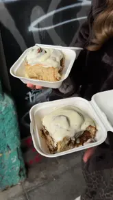 A fast-paced, vlog-style video featuring two creators reviewing cinnamon rolls from six different London bakeries as part of a series. The video follows a countdown format, showing the product, the venue exterior, and the presenters' reactions to each item.