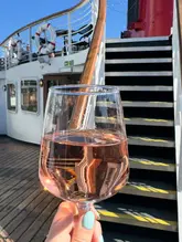 A bright, sunny shot of a glass of rosé wine held up against the deck of the Daffodil boat in Liverpool, capturing the essence of a relaxed day out.