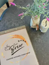 A clean, well-lit, and inviting shot of a menu on a table at The Barn Brew, accompanied by a small vase of flowers and a salt and pepper shaker, establishing a relaxed, countryside cafe atmosphere.