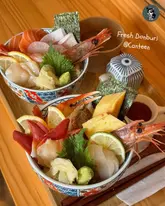 A bright, high-quality overhead shot of two Japanese donburi bowls featuring fresh sashimi, served with miso soup on a clean wooden table. The composition is balanced and the food presentation is highly appetising.