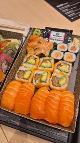 A promotional reel for Sushinoya in Cambridge, featuring shots of the shop exterior, chefs preparing fresh sushi, a display of pre-packaged sushi sets, and a customer enjoying the food and drinks.