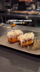A promotional video for a burger omakase experience in London, featuring close-up shots of the chef preparing various slider-sized burgers with a blowtorch and plating them, followed by shots of customers enjoying the meal.