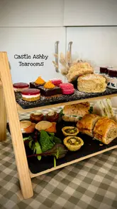 A montage video showcasing an afternoon tea service at The Castle Ashby Tearooms, featuring close-ups of the savory and sweet items, as well as shots of the venue's garden and interior, including a dedicated kids' play area.
