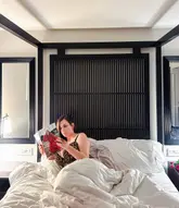 A lifestyle-focused influencer shot featuring a guest relaxing in a hotel bed at La Suite West, Hyde Park, promoting the venue's comfortable and aesthetic accommodation.