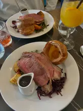 A high-angle, top-down shot of a Sunday roast dinner featuring sliced beef, a large Yorkshire pudding, and red cabbage, with a drink visible on the table.