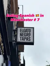 A static, low-angle shot of the El Gato Negro Tapas sign against a grey, overcast sky, used as part of a series documenting Spanish dining in Manchester.