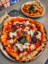 A top-down shot of a wood-fired pizza and a bowl of gnocchi on a grey table, likely taken in a restaurant setting.