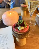 A beautifully composed, atmospheric close-up shot of an amuse-bouche served on a unique stone pedestal. The warm, candlelit background and shallow depth of field create an intimate, high-end dining ambiance, effectively highlighting the intricate plating of the dish.