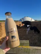 A bright, well-composed shot featuring a bottle of milkshake held in the foreground against a blurred background of a farm with calves. The image effectively captures the product and the setting, creating an inviting and wholesome atmosphere.
