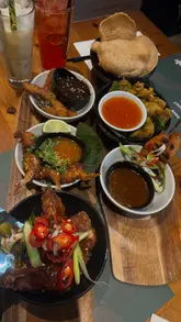 A montage of food and drink dishes from a Thai restaurant, including shots of the menu, cocktails, and various small plates like satay skewers, wings, and curry.