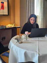 A lifestyle shot featuring a woman working on a laptop at a table in a hotel lounge, accompanied by a coffee and a croissant. The setting is elegant and quiet, emphasizing the hotel's atmosphere.