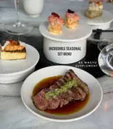 A high-quality, well-lit shot of a set menu spread at a restaurant, featuring a beautifully plated A5 Wagyu steak in the foreground and various appetizers in the background. The composition is clean and professional, effectively showcasing the premium nature of the food.
