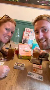A couple visits a board game cafe, showcasing the extensive games library, food, and cocktails, highlighting it as a great date night spot.