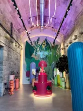 A wide-angle, symmetrical shot of the Edinburgh Gin Distillery interior, showcasing the vibrant, neon-lit, arched stone architecture and the central product display.