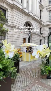 A short, aesthetic montage showcasing a pop-up collaboration between Magnolia Bakery and Café Ciel in London. The video features close-up shots of their signature banana pudding, matcha lattes, and cold brew coffee, set against the backdrop of a branded yellow-and-white striped stall decorated with flowers.