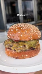 A short, engaging review of a burger restaurant called Milk Bun, featuring close-up shots of smash burgers, fries with cheese sauce, deep-fried pickles, and a cookie ice cream sandwich. The video captures the casual dining experience and the appetizing nature of the food.