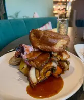A close-up, eye-level shot of a Sunday roast dinner featuring a large Yorkshire pudding, various meats, and gravy, served in a restaurant setting.