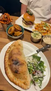 A promotional video showcasing a limited-time £5 burger and pizza deal at Frankie & Benny's. The video features close-up shots of various dishes including a double stack burger, a calzone, and loaded fries, accompanied by a voiceover explaining the offer and the dining experience.