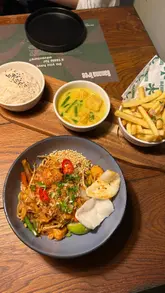 Here are a few options for your SEO alt text, depending on what the photo shows:

**Option 1 (Focus on the food):**
Table full of Thai food including satay skewers, pad thai, and curries at Banana Tree restaurant in Oxford.

**Option 2 (Focus on the experience):**
Two people sharing a variety of Thai-inspired bowls and mocktails during the Banana Tree Bottomless Bowls deal.

**Option 3 (Concise & keyword-rich):**
Selection of Thai dishes like veggie satay and pad thai from the Banana Tree Bottomless Bowls menu in Oxford.

**SEO Tip:** If the photo shows a specific dish (like the skewers or pad Thai) as the main focus, use that in the description instead of "Thai dishes.