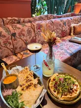 A high-quality, inviting shot of a brunch spread featuring quesadillas, a waffle dish, and two cocktails, set against a stylish, patterned booth background.